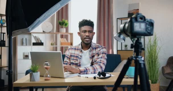 Kamera fotografowania sympatyczny pewny siebie nowoczesny młody czarny skóry mężczyzna IT pracownik, który wyjaśnia, jak korzystać z programów komputerowych podczas transmisji online dla publiczności internetowej — Wideo stockowe