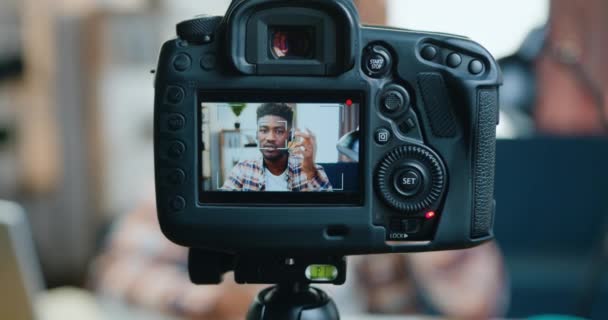Ver a través de la lente de la cámara de buen aspecto moderno éxito de piel negra blogger masculino en los auriculares de grabación de nuevo vlog para sus espectadores de Internet — Vídeos de Stock