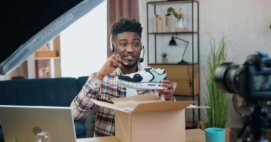 Blog yazma, alışveriş ve sunum konsepti, kameraya yeni alınmış spor ayakkabıları paketlerini açan, tatmin edici, siyah derili, erkek blog yazarı