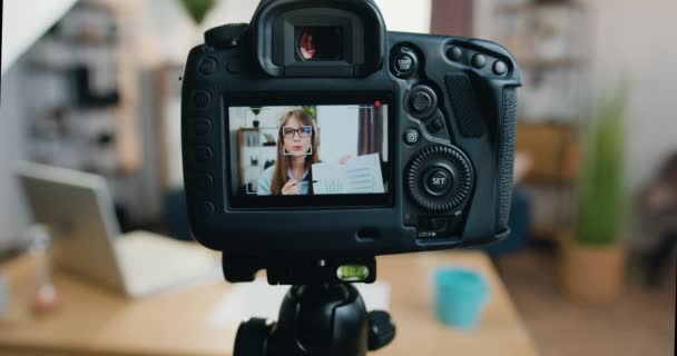 Φωτογραφική μηχανή λήψης του όμορφου αυτοπεποίθηση έξυπνο σύγχρονο κορίτσι σε ακουστικά που καταγράφουν βίντεο για το κοινό στο διαδίκτυο και εξηγώντας τα αποτελέσματα της έρευνάς της — Αρχείο Βίντεο