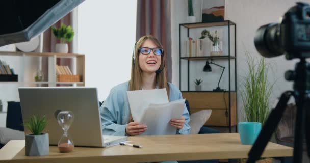 Hermosa persona femenina satisfecha experimentada de 25 años en auriculares vomitando informes financieros durante la celebración de webinar en línea en la cámara y saludando a su audiencia con éxito terminando su curso — Vídeo de stock