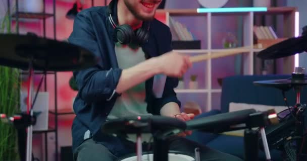 Красивий усміхнений задоволений професійним 25-річним барабанщиком, насолоджуючись грою на барабанах в домашній студії в вечірній час, концепція ліцею — стокове відео