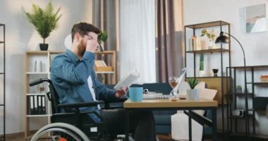 Evde geçirdiği kazadan sonra tekerlekli sandalyede oturan ve gözlüğünü takıp ilginç kitap okumaya ve çay içmeye devam eden sevimli, konsantre olmuş sakallı bir adam.