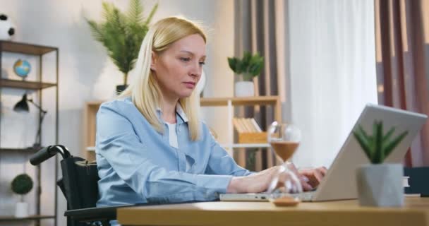 Atractiva mujer de negocios profesional moderna concéntrica sentada en silla de ruedas después de un accidente y trabajando en la computadora en casa durante el día — Vídeo de stock