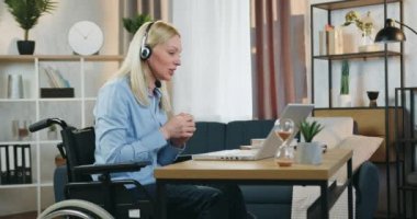 Evde geçirdiği kazadan sonra tekerlekli sandalyede oturan ve izleyicileri için internetten giydiği kulaklıkla kendine güvenen iyi görünümlü profesyonel kadın koçun yan görüntüsü.