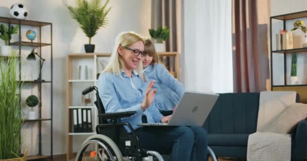 Modern teknik koncept där attraktiva leende glad funktionshindrade kvinna i glasögon och hennes 10-åriga glada dotter njuter av trevlig videochatt med släktingar på datorn hemma — Stockvideo