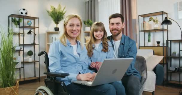 Attractive smiling loving bearded father,his cute 10-aged positive daughter and pretty satisfied ,temporarily confined to a wheelchair after acccident,wife together applying laptop to revision — Stock Video