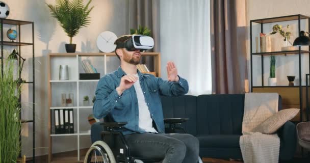 Достойный доверия высококвалифицированный бородатый инвалид в инвалидной коляске носит наушники виртуальной реальности, работающие на воображаемом дисплее дома — стоковое видео