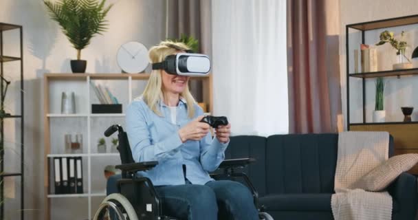 Όμορφη ευτυχισμένη ικανοποιημένη γυναίκα με ανοιχτά μαλλιά σε αναπηρική καρέκλα με γυαλιά επαυξημένης πραγματικότητας απολαμβάνοντας βιντεοπαιχνίδια και γιορτάζοντας τη νίκη με τα χέρια ψηλά — Αρχείο Βίντεο