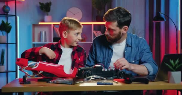 Attractive curious teen boy trying to touch details of driven toy car when his attantive caring bearded father beating him on hand not to touch without permission — Wideo stockowe