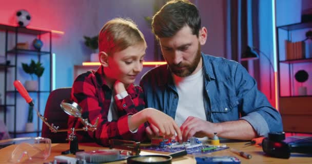 Pleasant high-skilled smiling 35-aged bearded man collecting small details of constructor to light the lamp and curious teen son is surprised from seen result — Stock video