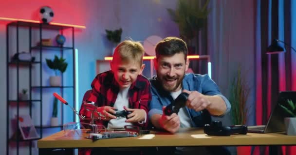 Joyeux garçon heureux émotionnel de 12 ans célébrant la victoire sur son père barbu insatisfait dans les jeux vidéo à la maison le soir, au ralenti — Video