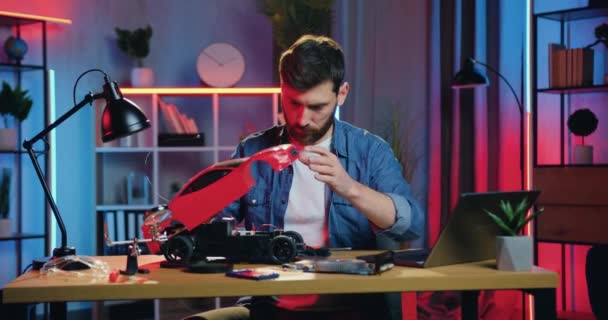 Attraktiv selvsikker alvorlig dygtig skægget mand, der tager legetøjsvogne toppen og lærer indholdet af det, før du reparerer hjemme om aftenen, menneskeligt hobbykoncept – Stock-video