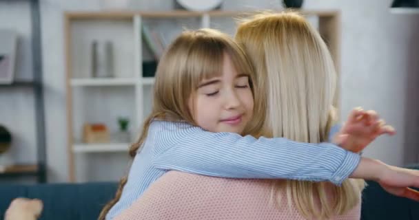 Close up de muito sorrindo feliz mulher de cabelos claros que posando com as costas na câmera durante abraços com sua filha de 12 anos alegre bonito em casa — Vídeo de Stock
