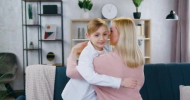 Güzel dekore edilmiş oturma odasında 35 yaşındaki güzel annesiyle kucaklaşan 10 yaşında yakışıklı bir çocuğun portresi.