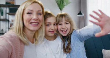 Güzel, mutlu, güler yüzlü, sevgi dolu anne ve onun iki çocuğu ve kızı güzel dekore edilmiş oturma odasında tatmin olmuş yüz ifadeleriyle selfie çekiyorlar.
