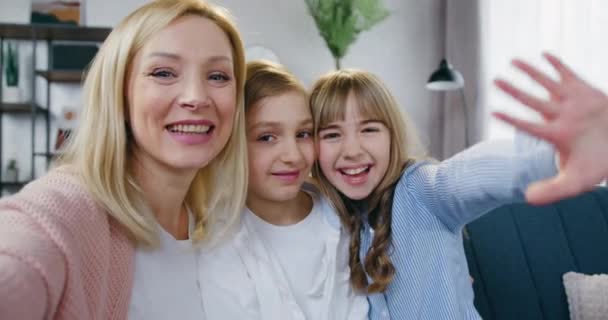 Güzel, mutlu, güler yüzlü, sevgi dolu anne ve onun iki çocuğu ve kızı güzel dekore edilmiş oturma odasında tatmin olmuş yüz ifadeleriyle selfie çekiyorlar. — Stok video