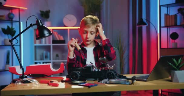 Aantrekkelijke attente nieuwsgierige tiener jongen zitten in de voorkant van zijn gebroken speelgoed auto en proberen om kleine details vast te stellen met soldeerbout — Stockvideo
