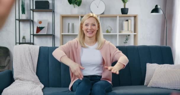 Schöne glücklich lächelnde liebende Frau, die auf der Couch im modernen Wohnzimmer sitzt und ihre Kinder umarmt, die mit glücklichen Gesichtern auf sie zustürmen — Stockvideo