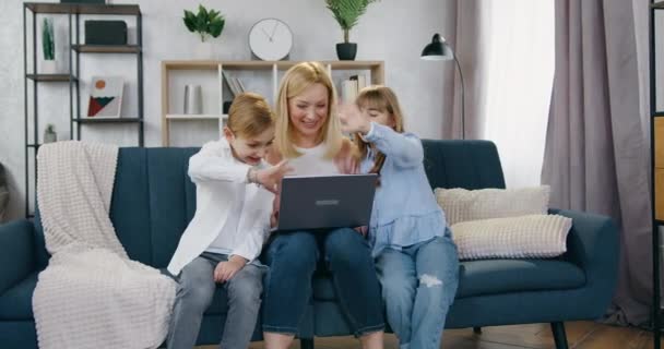 魅力的な笑顔幸せな光髪の母親座っていますオンザカウチとともに彼女の陽気な息子と娘とともにビデオチャット中に夫,フロントビュー — ストック動画
