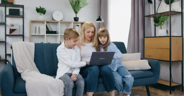 Härligt glad glad leende ljushårig mor och hennes positiva son och dotter sitter tillsammans på soffan i mysiga vardagsrum under videochatt med släkting på datorn — Stockvideo