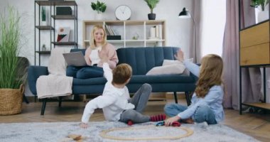 Sevimli, oyuncu, 12 yaşında erkek ve kız kardeş araba raylarıyla oynarken eğleniyorlar ve koltukta bilgisayar başında çalışan mutlu annelerine merhaba demek için el sallıyorlar.