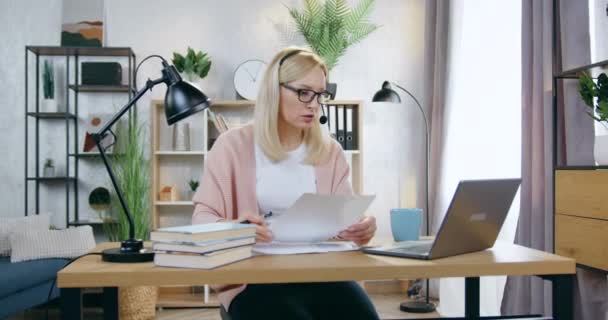 Όμορφη αυτοπεποίθηση υπεύθυνη ειδικευμένη ξανθιά γυναίκα με ακουστικά σε γυαλιά διεξαγωγή τηλεδιάσκεψης στο φορητό υπολογιστή από όμορφα διακοσμημένα γραφείο στο σπίτι — Αρχείο Βίντεο
