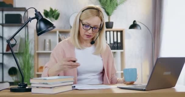 Attraente responsabile laboriosa donna di 35 anni in occhiali che lavora a casa scrivania con documenti e informazioni sul computer contemporaneamente bere tazza di tè — Video Stock