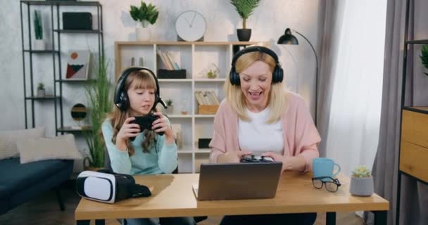 Υπέροχο χαρούμενο χαμογελαστό έφηβο κορίτσι γιορτάζει τη νίκη επί της όμορφης σε καλή διάθεση ξανθά μητέρα της, όταν ανταγωνίζονται μαζί σε βιντεοπαιχνίδια στον υπολογιστή στο σπίτι — Αρχείο Βίντεο