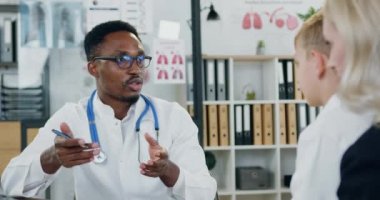 Yakışıklı, kendine güvenen, siyah tenli erkek doktor çocuk ve ilgili annesiyle özel kliniğe yaptıkları ziyarette konuşuyor.