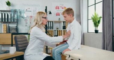 Güzel, yetenekli sarışın kadın-doktor. Kalp atışlarını ve akciğerlerini kontrol ediyor. Genç, sakin bir çocuk.