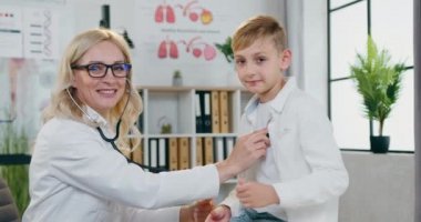 Sağlık sigortası konsepti, gülümseyen, açık renk saçlı bir kadın doktorun genç erkeklerin akciğerlerini kontrol etmesi ve birlikte kameraya iyi iş çıkarmaları.
