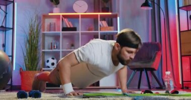 Sağlıklı yaşam tarzı konsepti. Akşamları iyi görünümlü, aktif, genç ve sakallı bir adamın evde antrenman yaparken yerden şınav çekmesi.