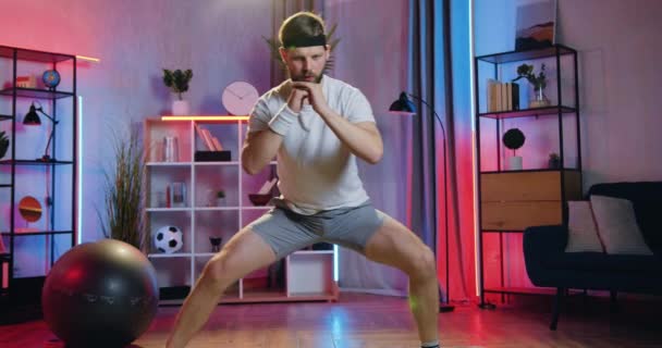 Přední pohled na dobře vypadající sebevědomý aktivní svalnatý vousatý chlap ve sportovním oblečení, který dělá sportovní cvičení doma během večerního tréninku — Stock video