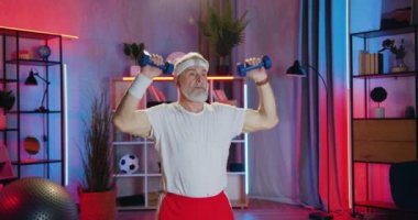 Spor giyimli 70 yaşındaki spor sakallı, güzel görünümlü sporcunun portresi. Akşam antrenmanı sırasında dambıllarla egzersiz yapıyor.