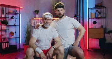 Yakışıklı, güler yüzlü, aktif, sakallı, son sınıf dedesi ve spor bahislerindeki küçük torunu ev ödevi sırasında kamera önünde baş parmaklarıyla poz veriyorlar.