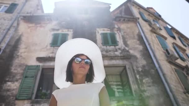 Szczelnie uśmiechnięta młoda, szczęśliwa kobieta w słomkowym kapeluszu w okularach przeciwsłonecznych spacerująca po starym mieście. Na zewnątrz — Wideo stockowe