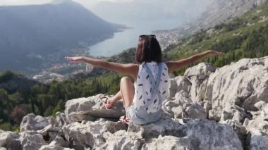 Deniz seviyesindeki kayaların üstünde oturan genç bir kadın el kaldırdı. Güzel manzaranın ve yaz rahatlığının tadını çıkarıyordu.