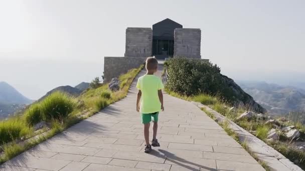 Вид сзади симпатичного мальчика 5 лет, идущего на вершине по каменной дорожке, чтобы увидеть красивый пейзаж Монтенегро — стоковое видео