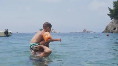 5-7 yaşlarındaki küçük bir çocuk yaz tatilinde babasının omzunda takla attırıyor.