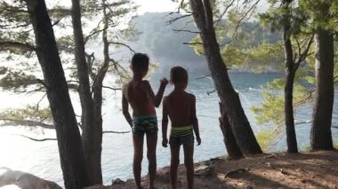 5 ve 7 yaşlarındaki iki çocuğun yüksek kayalıklarda durup yaz tatili boyunca denize hayran bakışları..