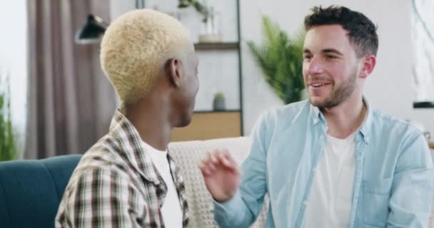 Concept de relation homosexuelle où attrayant souriant heureux jeunes gays de race mixte embrassant tendrement l'autre assis sur le canapé à la maison — Video