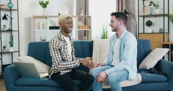 可爱的笑着爱着快乐的多种族同性恋夫妇坐在家里的沙发上，温柔地拥抱彼此，充满爱心和承诺 — 图库视频影像