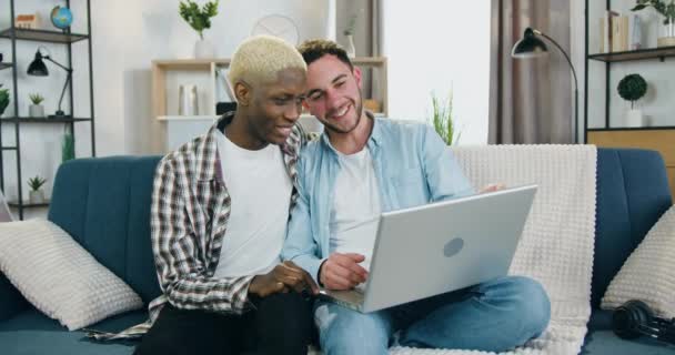 Concepto de comunidad LGBT donde la pareja gay de raza mixta sonriente feliz y guapa ama pasar su tiempo libre en casa y usar la computadora — Vídeos de Stock