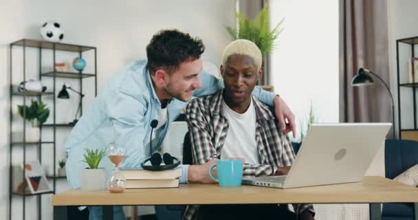 Retrato de pareja homosexual multirracial enamorada donde disfrutan de la comunicación conjunta en casa mientras aplican la computadora, cámara lenta — Vídeo de stock