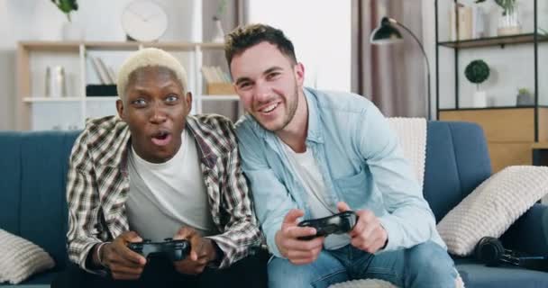 Homossexual conceito de lazer onde atraente feliz sorrindo amoroso diverso casal gay jogos com joysticks em casa, um deles perdeu o jogo, outro se alegrando da vitória — Vídeo de Stock