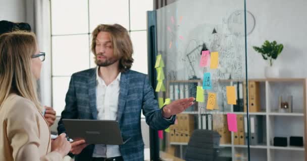 Office-Workflow-Konzept attraktiver lächelnder, erfolgreicher und erfahrener Mitarbeiter, die kreative Ideen des Gründungsprojekts in der Nähe von Glaswänden mit Aufklebern lebhaft diskutieren — Stockvideo
