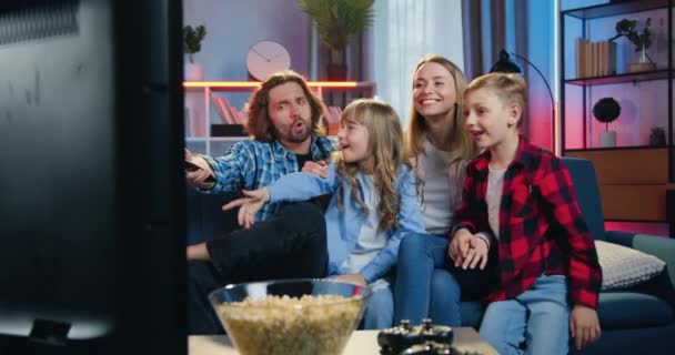 Human reaction of likable funny joyful kids which sitting on the sofa together with their parents and shouting when father changing channels using remote control — Stock Video