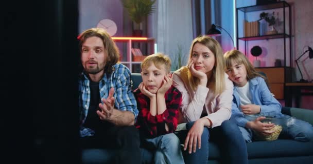 Urocza zdenerwowana przyjazna rodzina czterech osób-matka, ojciec, syn i córka oglądający znudzony film w telewizji w domu wieczorem i omawiający wydarzenia między sobą — Wideo stockowe