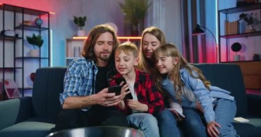 Güzel görünüşlü, güler yüzlü modern aile akşamları evdeki kanepede dinlenirken sakallı babam cep telefonuyla herkese nasıl oyun oynadığını gösteriyor.
